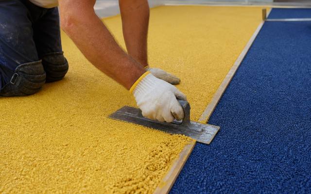 Yellow and navy playground rubber surfacing being hand-troweled at a daycare yard.