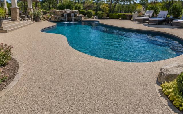 Backyard pool deck in sand-coloured rubber surfacing beside a stone waterfall feature.